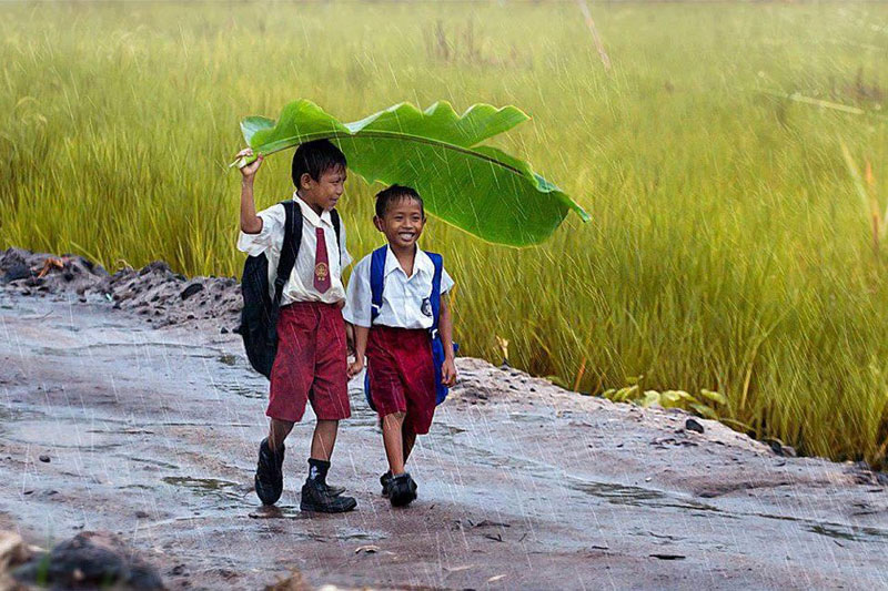 two-kids-under-a-banana-leaf-in-the-rain-indonesia